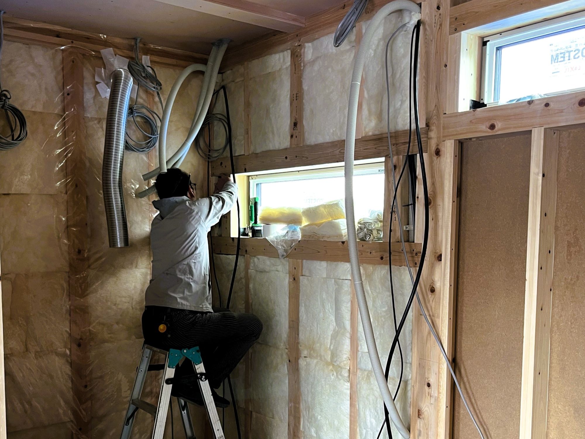 窓まわりで配線と配管を処理しながら気密施工を行っている現場の様子