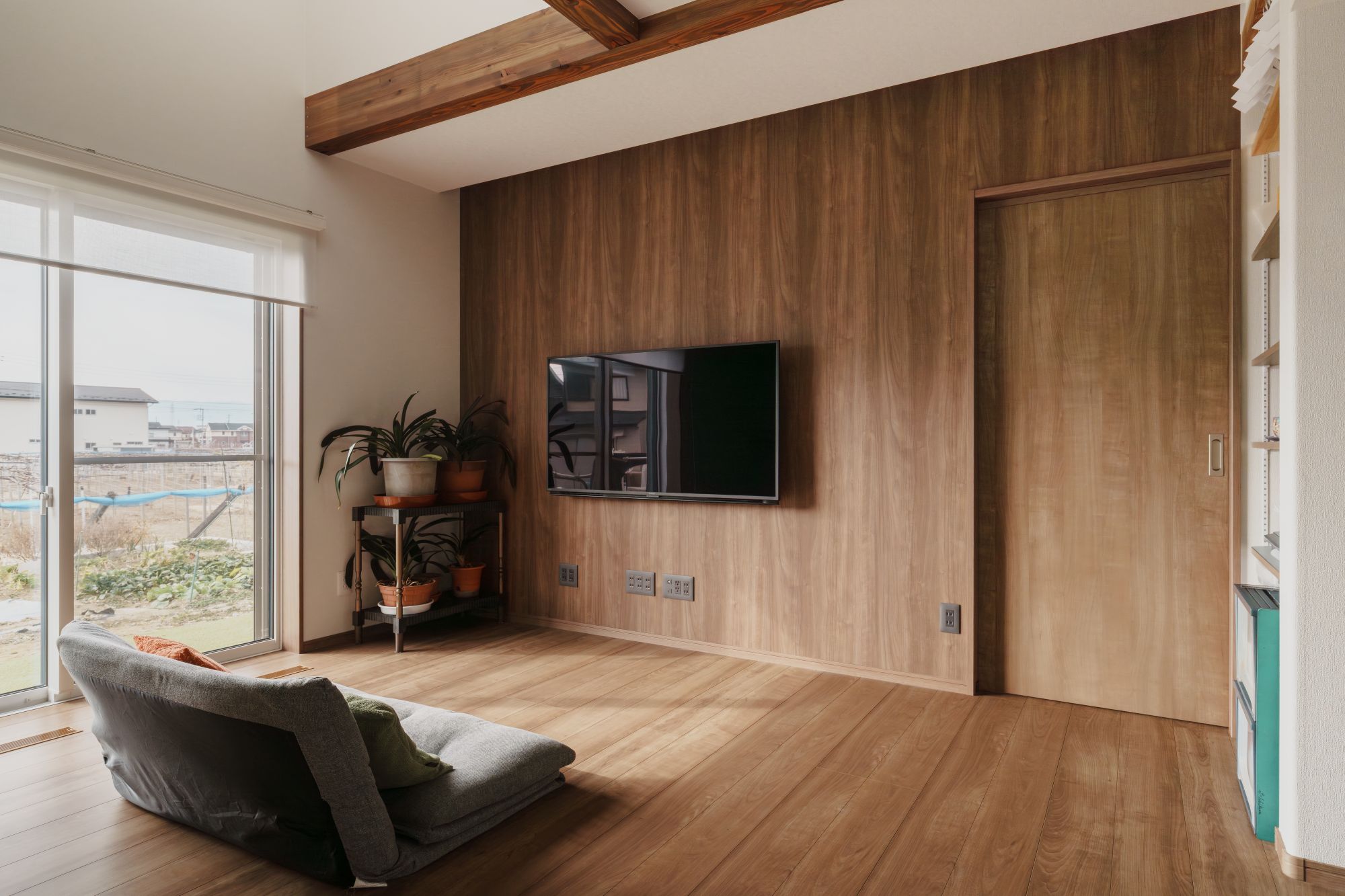 木目のテレビ背面壁と建具が並ぶリビングの内観
