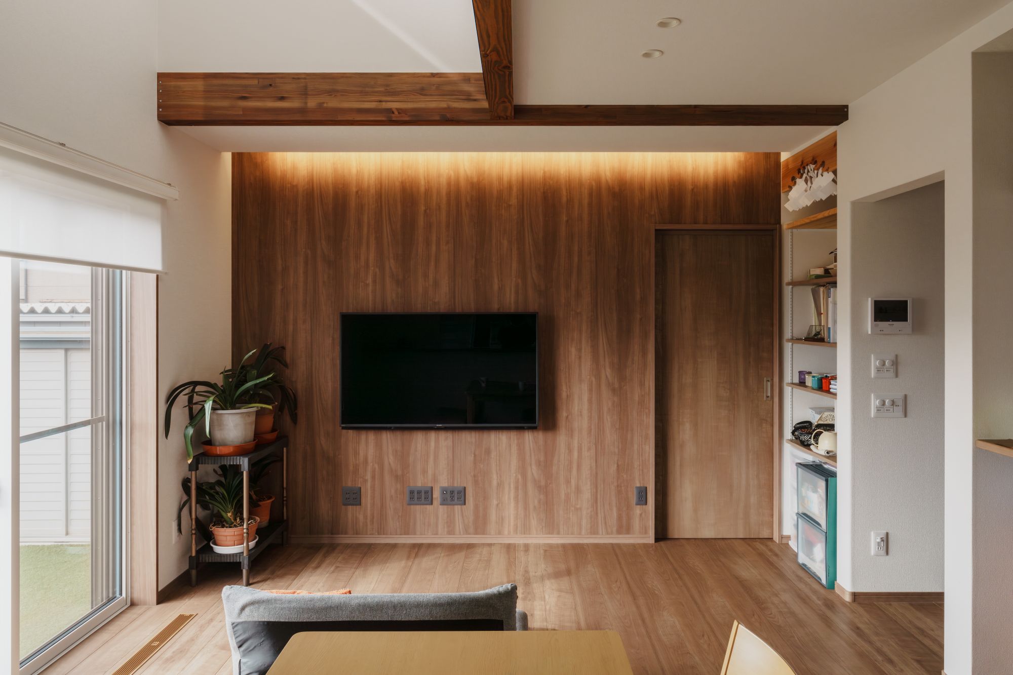 間接照明で木目壁を照らしたテレビ背面のリビング内観