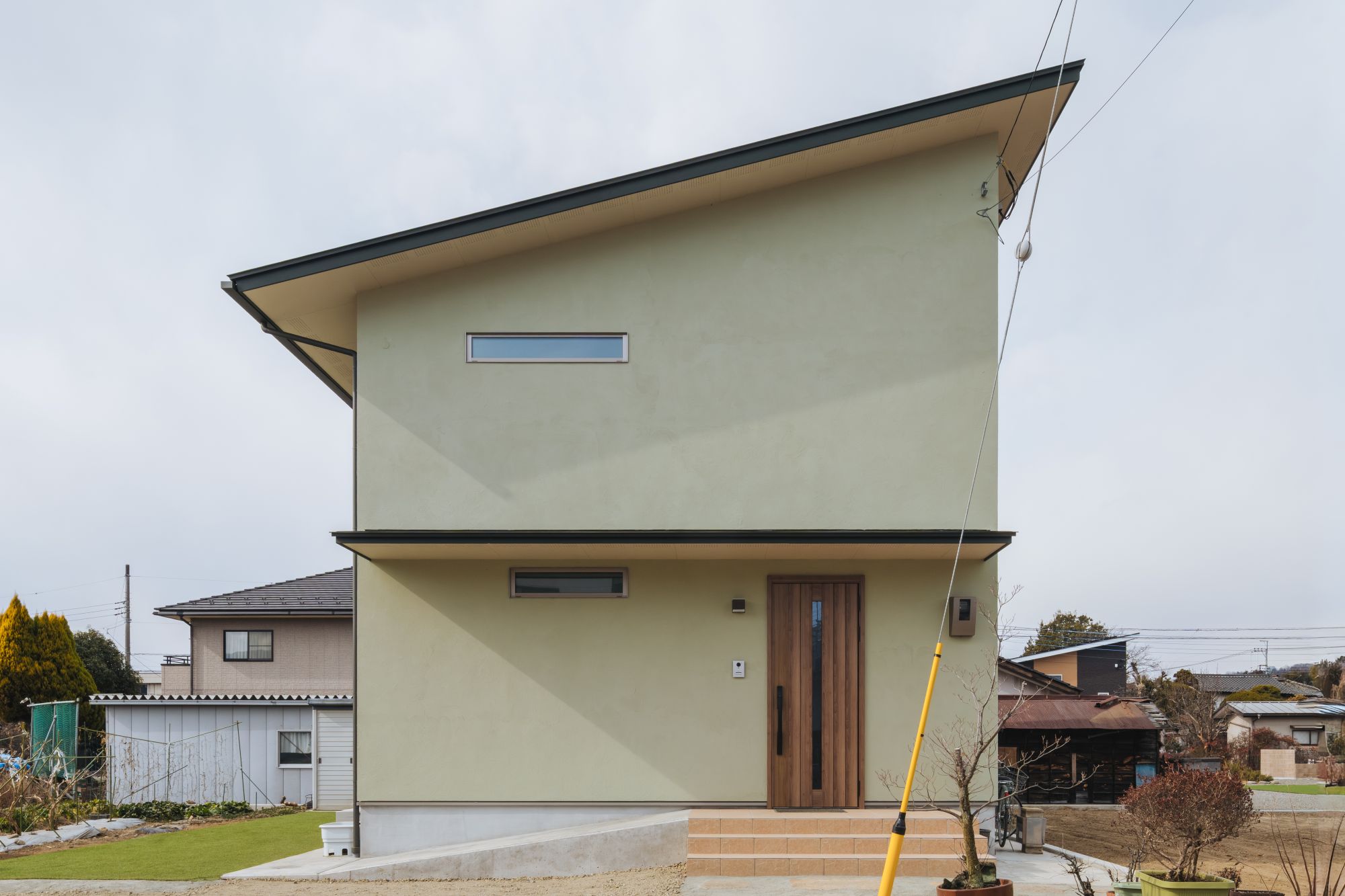 淡いグリーンの外壁と木製玄関ドアの正面外観