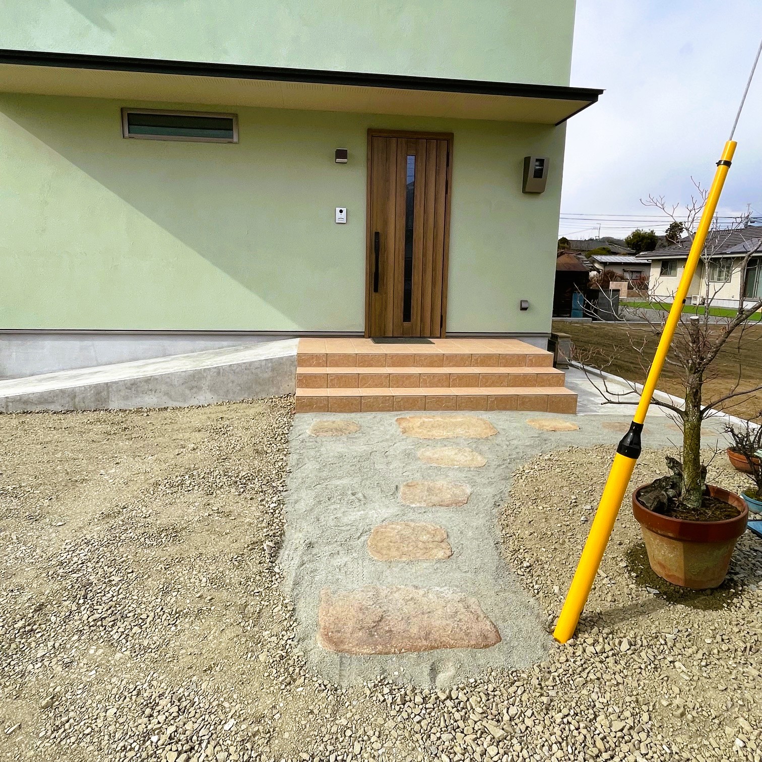 淡いグリーンの外壁と木製玄関ドア、自然石アプローチの外観全体