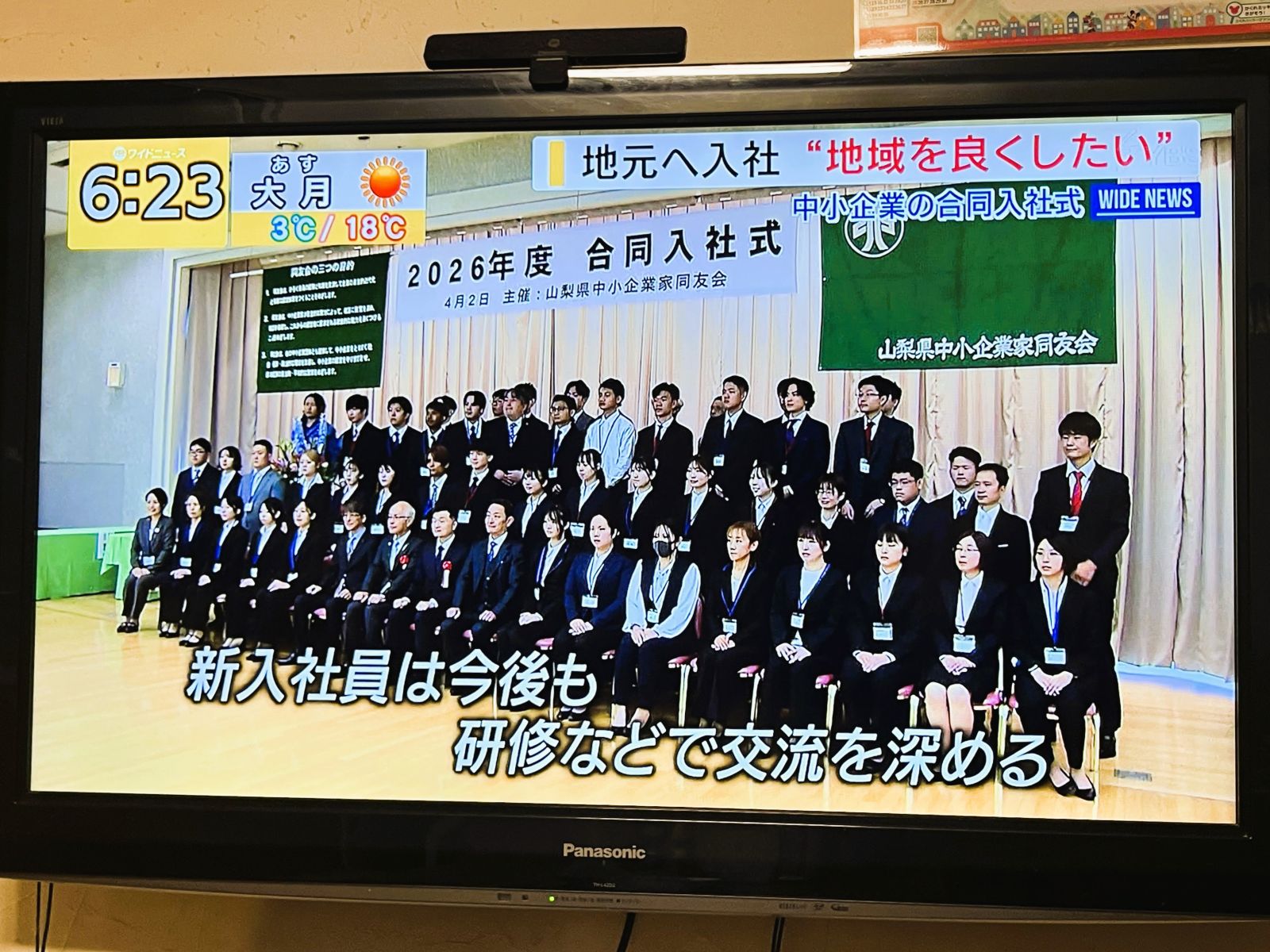 山梨県中小企業家同友会の合同入社式の集合写真がテレビニュースで紹介された画面