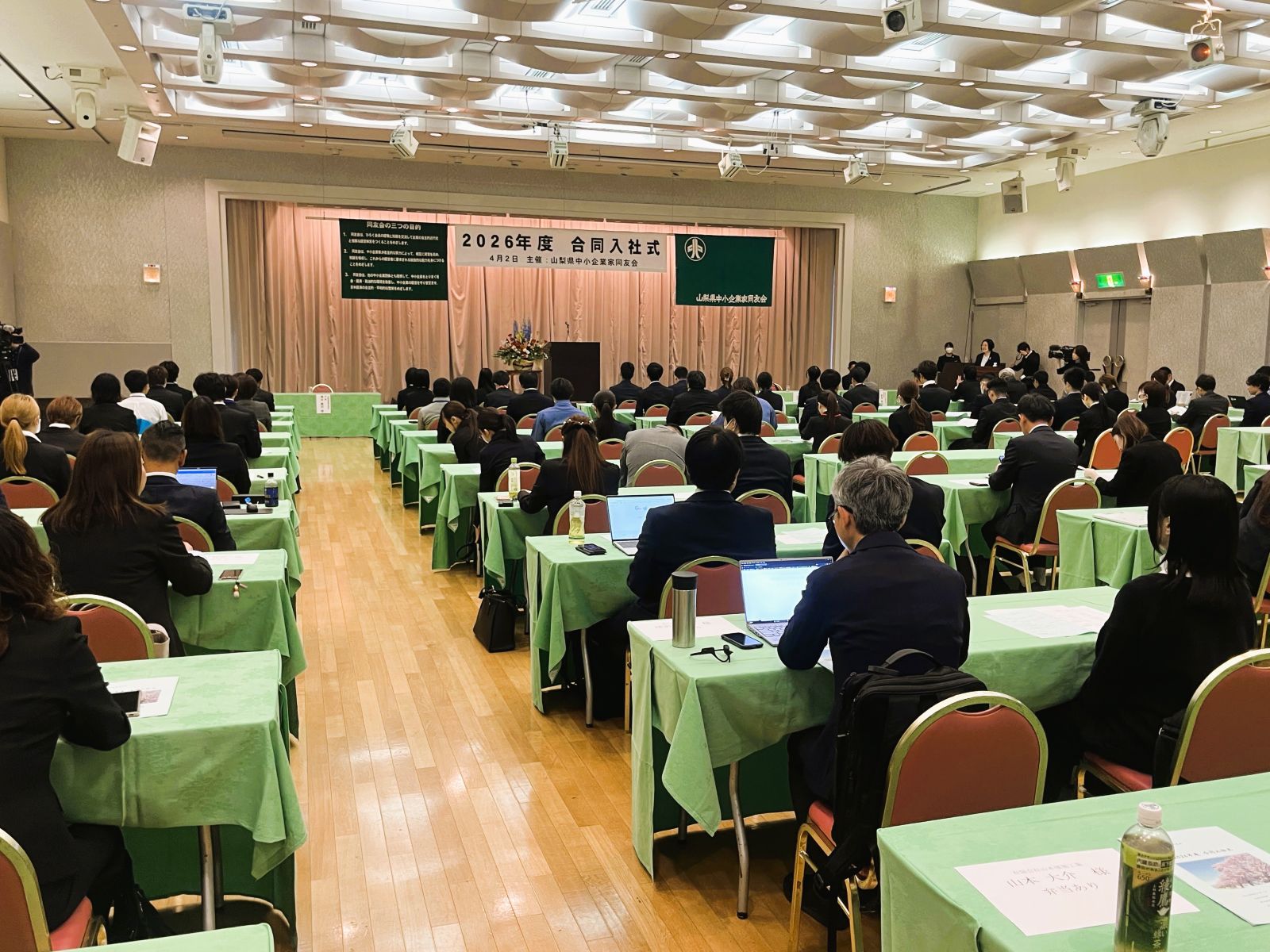 山梨県中小企業家同友会の2026年度合同入社式会場全景と参加者の様子