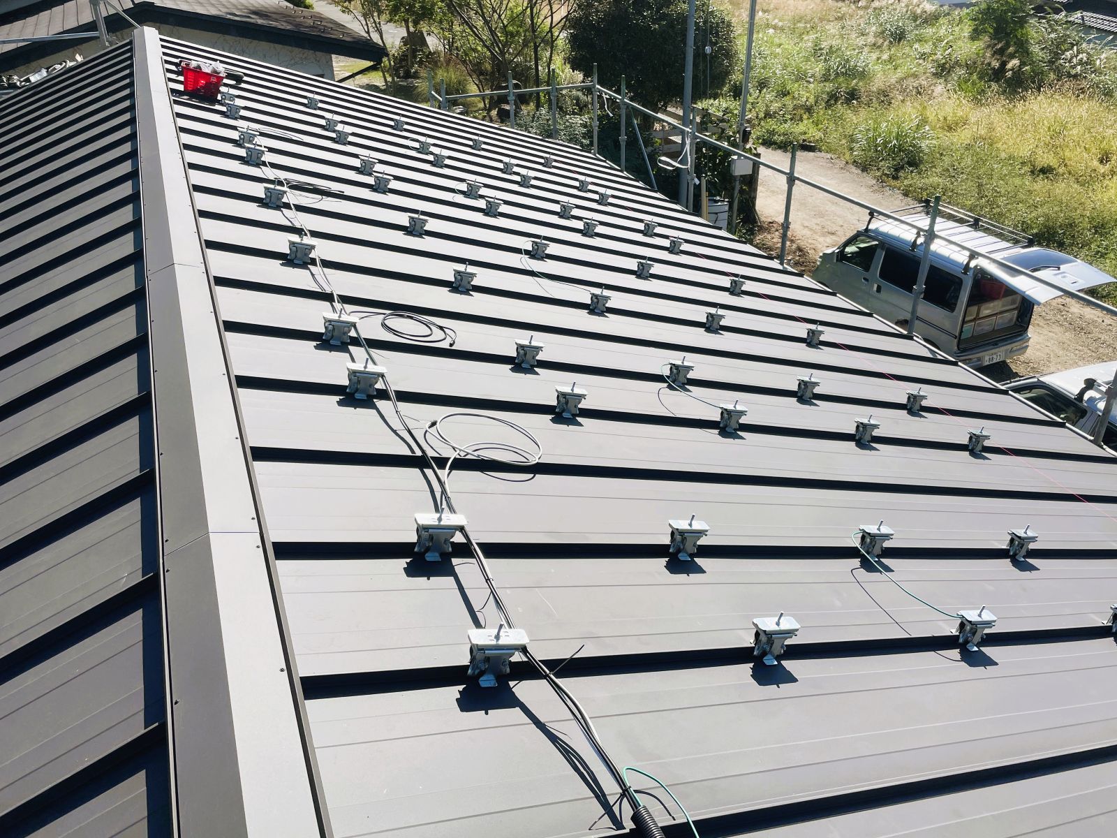 立平葺き屋根で太陽光発電パネル設置前の配線と支持金具施工を進めている様子
