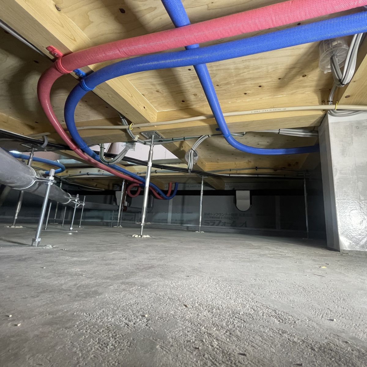 床下で大引きから吊られた給排水配管と点検スペース