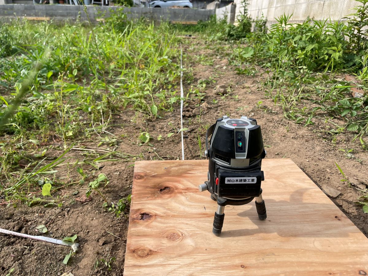 水平に調整した基準板へレーザーを据え、建物の通り芯と直角を確認している様子