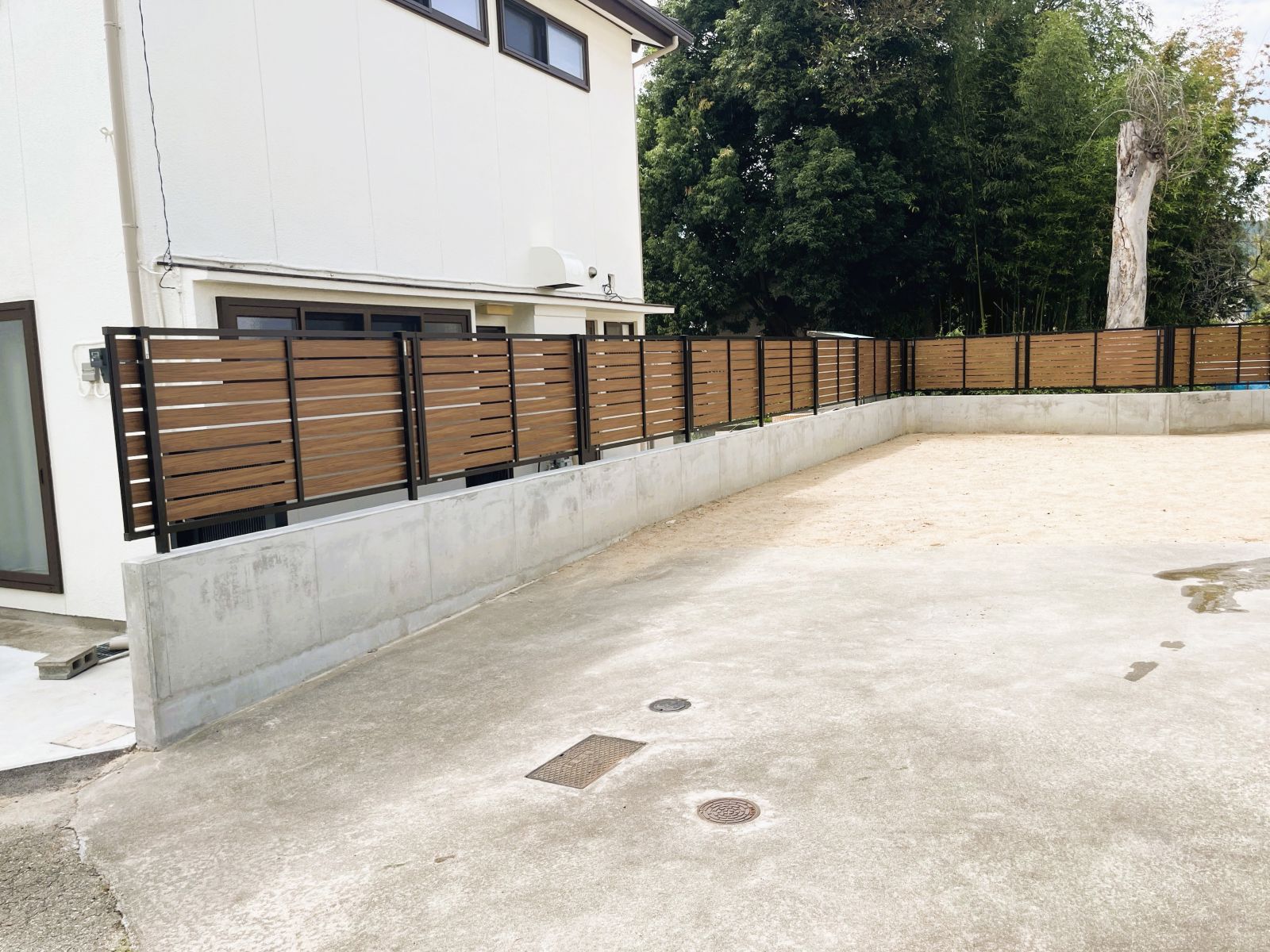 敷地の形に沿って木目調の目隠しフェンスを連続して設置した外構改修後の全景