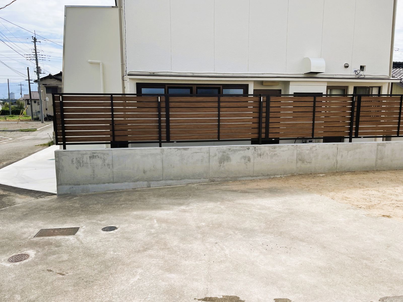 コンクリートの立ち上がりに木目調の目隠しフェンスを設置した外構改修後の道路側からの様子