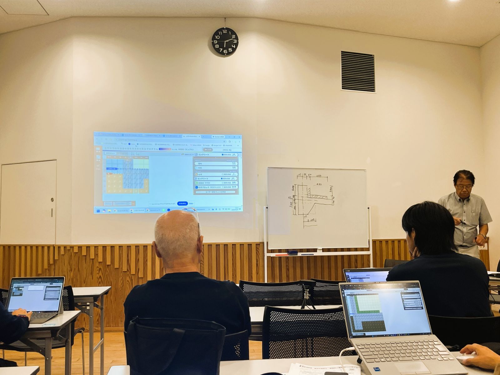 中村伊伯会長が基礎断面をホワイトボードに描き、線熱貫流率算出プログラムを説明している様子