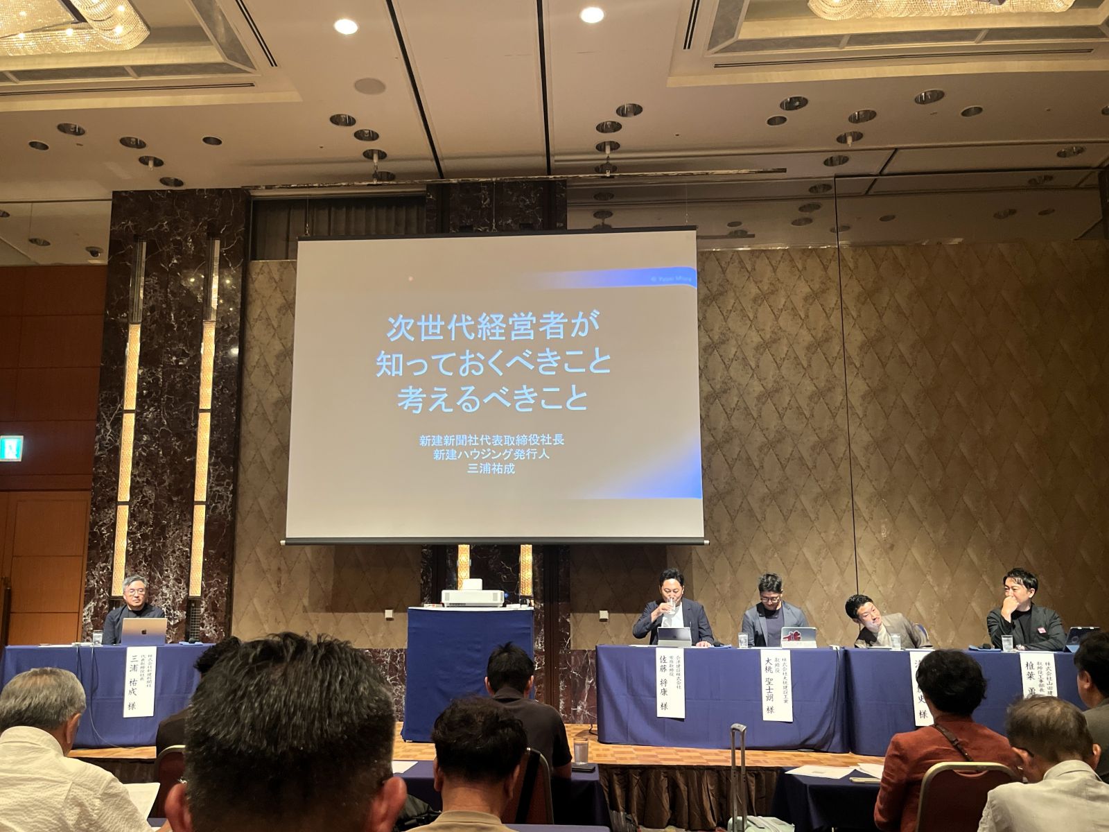 次世代経営者をテーマとする分科会の演題が映されたスクリーンと登壇者席の様子